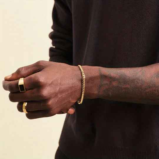 Person wearing gold rings and a bracelet on a neutral background