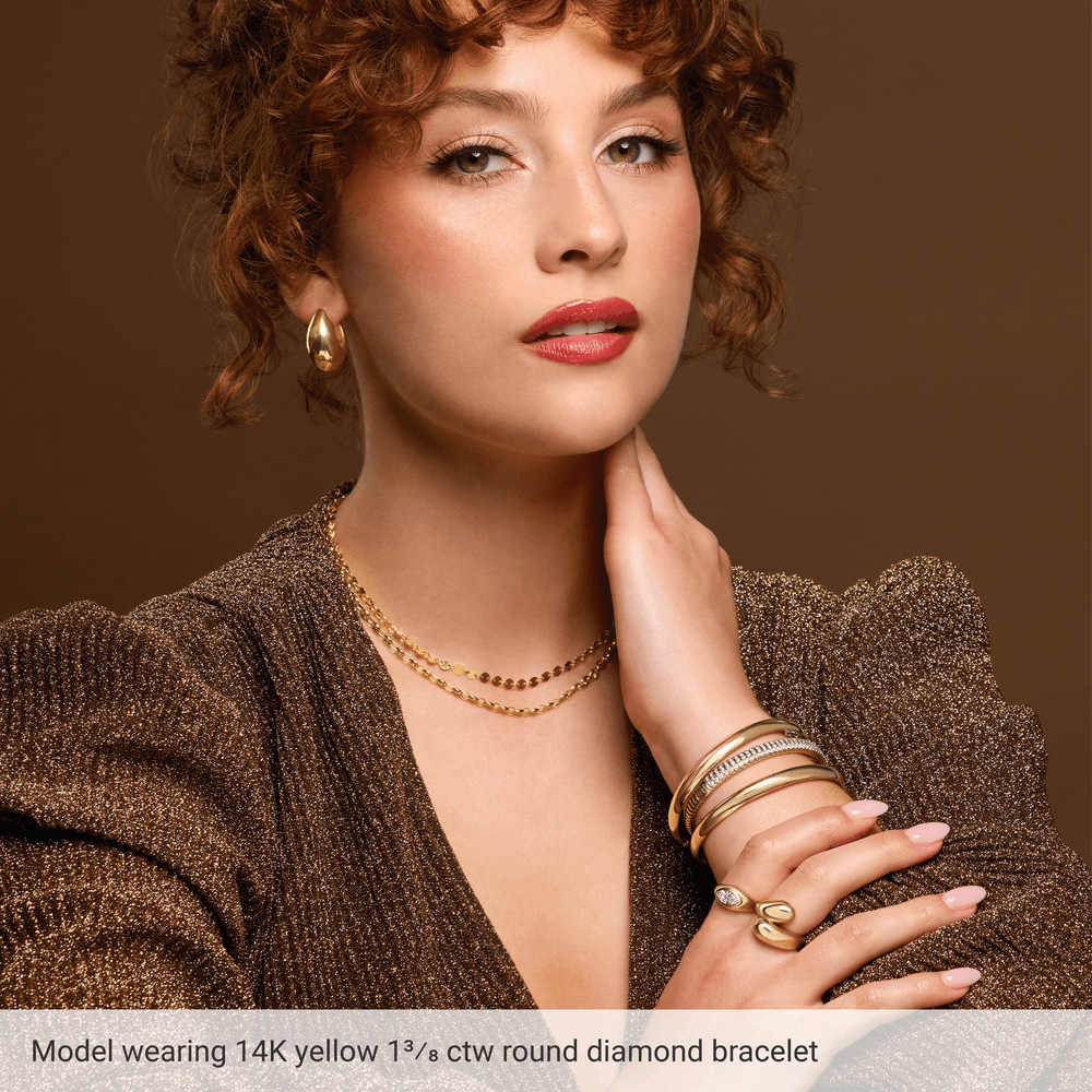 Woman wearing gold jewelry including a bracelet, necklace, and rings on a brown background