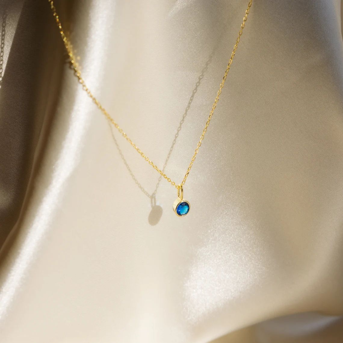 Gold necklace with a blue gemstone pendant on a beige fabric background