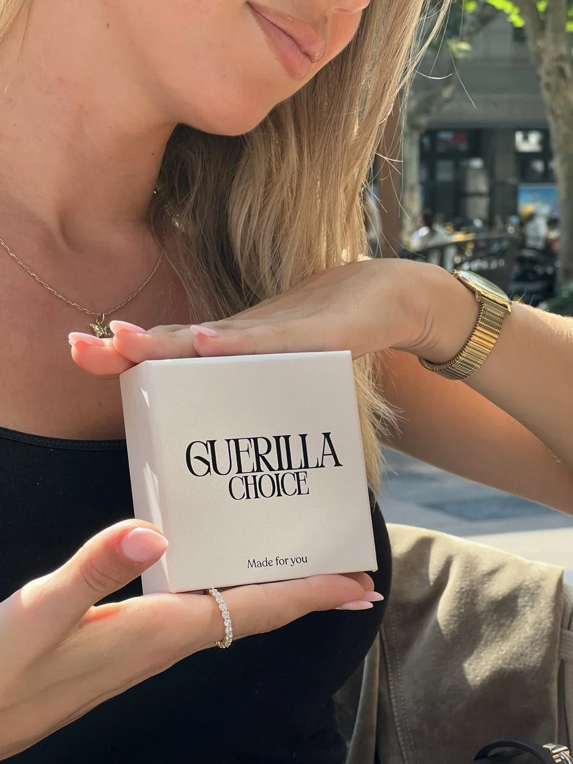Woman wearing a butterfly pendant necklace and sparkling ring with a black top, holding a Guerilla Choice box.
