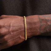 Gold bracelet on a wrist with tattoos against a dark background