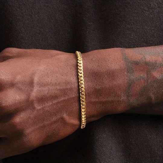 Gold bracelet on a wrist with tattoos against a dark background
