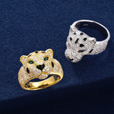 Two leopard-shaped rings, one gold and one silver, on a dark blue background.