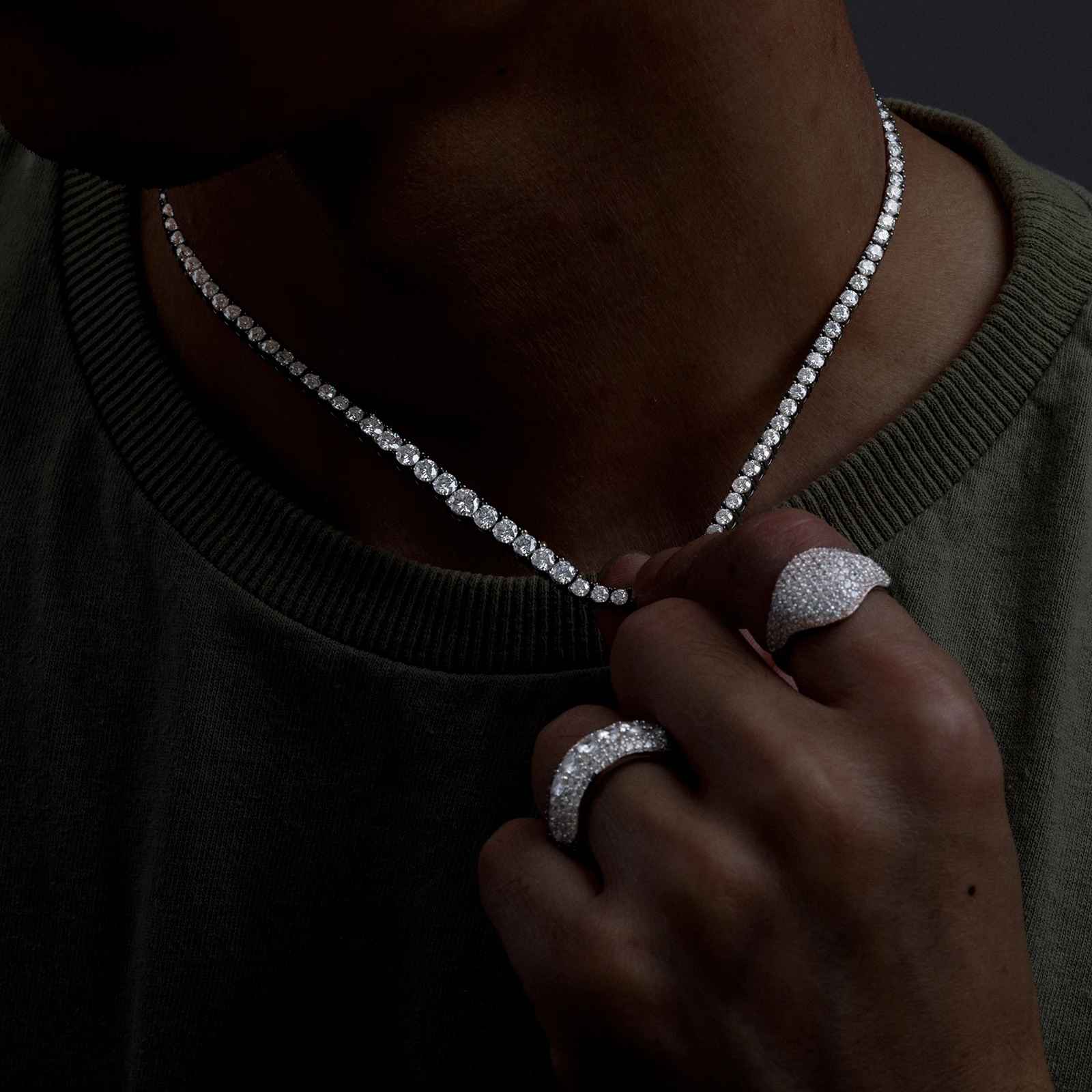 Person wearing a diamond necklace and rings on a dark background