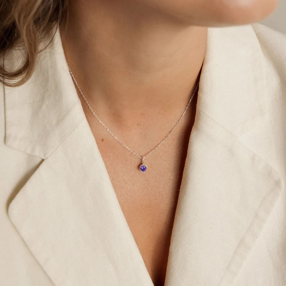 Necklace with a purple gemstone worn by a person in a beige blazer.
