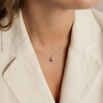 Necklace with a purple gemstone worn by a person in a beige blazer.