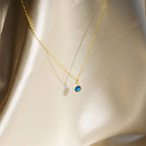 Gold necklace with a blue gemstone pendant on a beige fabric background