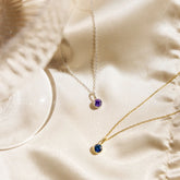 Two gold necklaces with gemstones on a beige fabric background