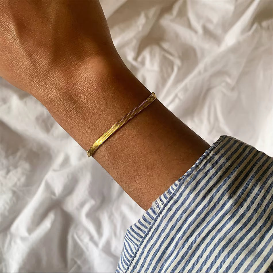 Gold bracelet on a wrist with a striped shirt sleeve against a white background