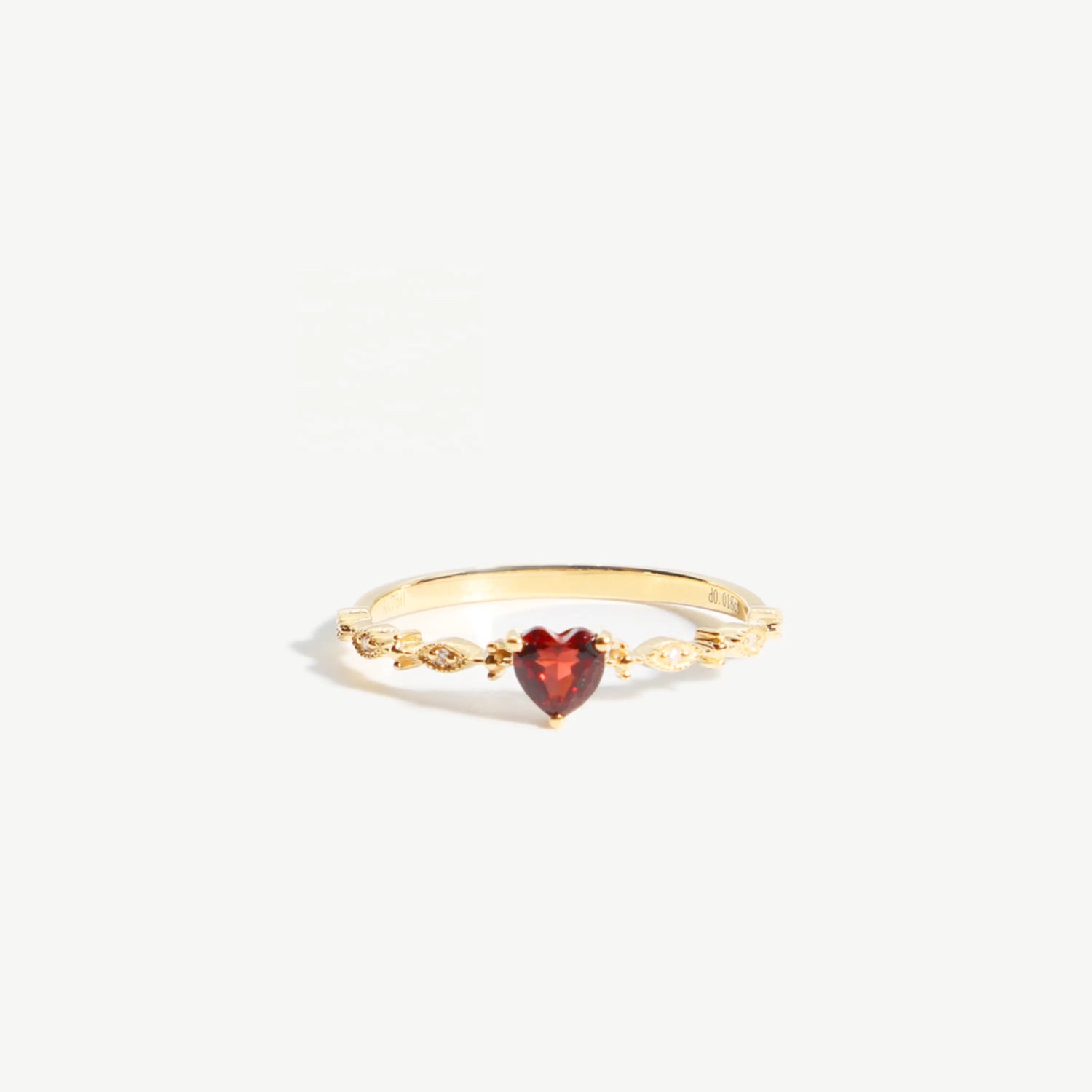 Gold ring with a heart-shaped red gemstone on a white background